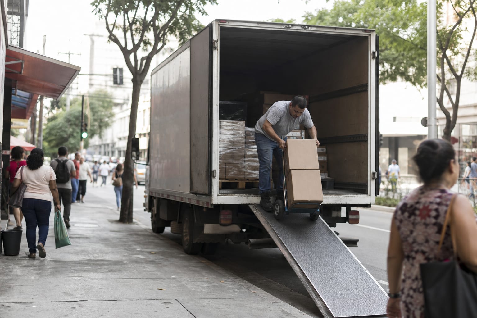 Caminhão de entrega urbano em vaga de carga e descarga com ajudante descendo caixas em rua de comércio