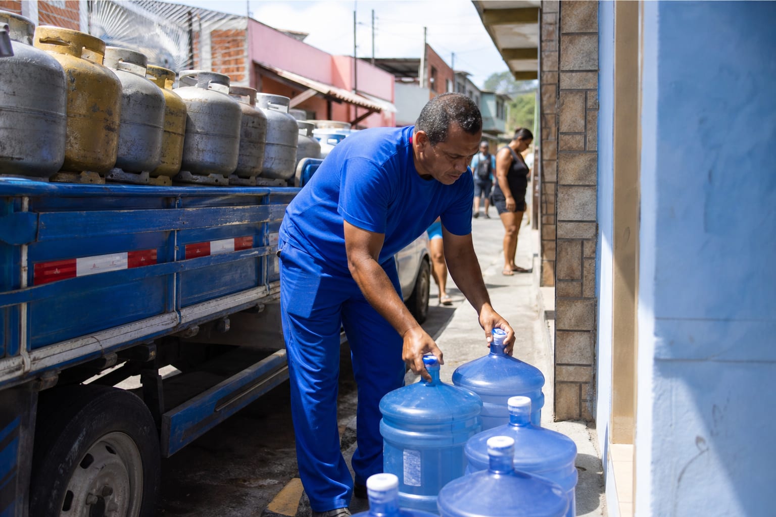 Entregador descarregando garrafões de água de vinte litros em frente a um mercadinho de bairro